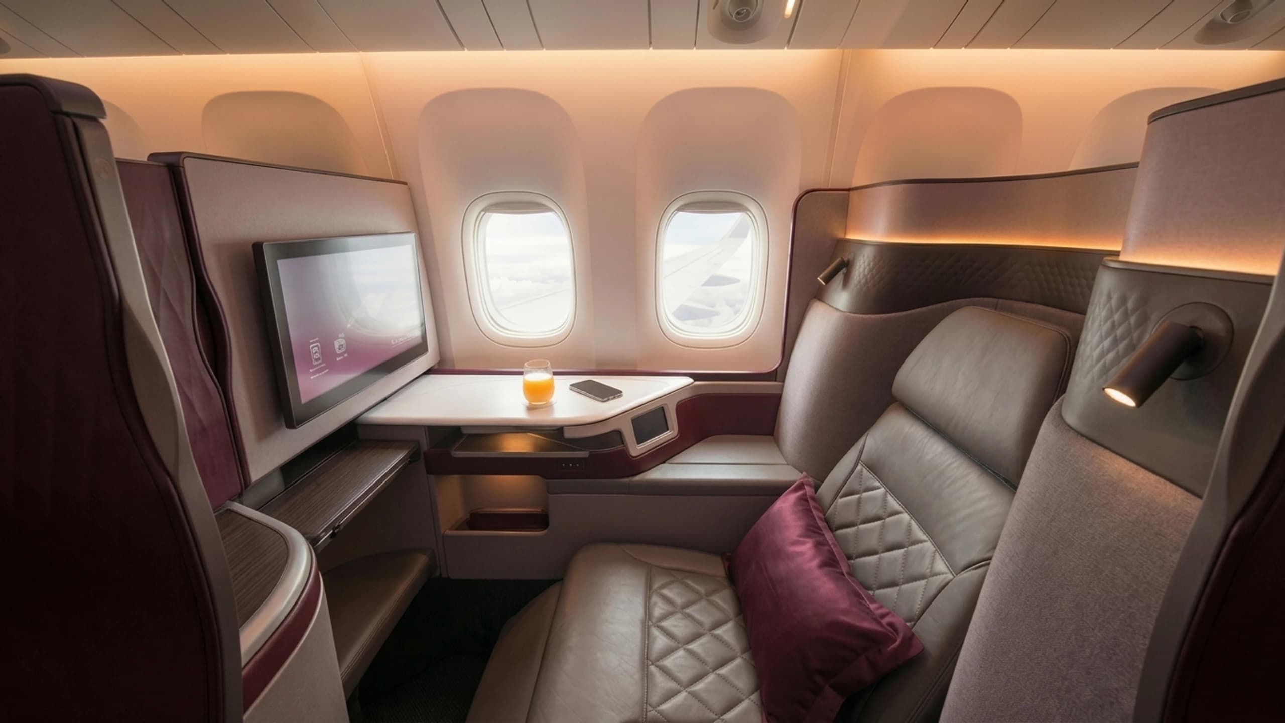 Luxury business class suite with diamond-stitched leather seating, dual windows, and burgundy accents